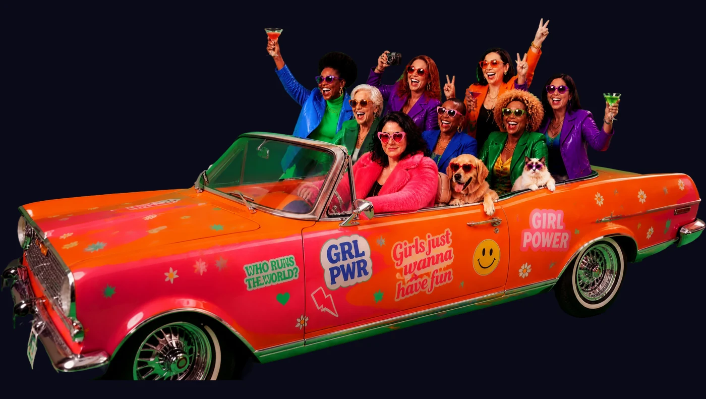 Huit femmes de tous âges et toutes origines dans un cabriolet orange couvert de stickers Girl Power, avec un chien et un chat, la communauté IAelle